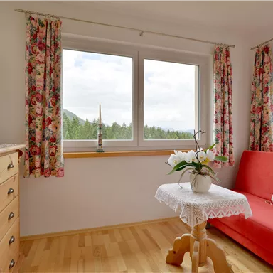Ein gemütlicher Wohnraum mit einem roten Sofa und einem kleinen Tisch. Die großen Fenster bieten einen Blick auf die Natur.