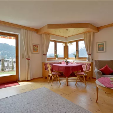 A cozy living room with a round dining table and a view of the mountains. Large windows let in plenty of light and create an inviting atmosphere.
