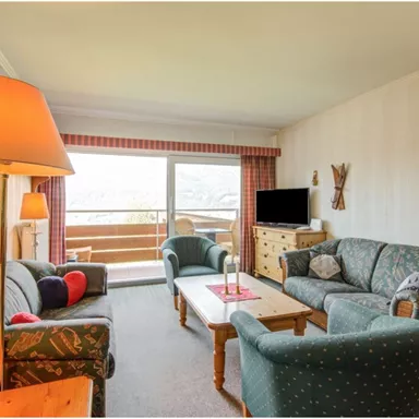 Ein gemütliches Wohnzimmer mit gemütlichen Sofas und einem Holztisch. Große Fenster bieten einen Blick auf die Terrasse und die Landschaft.