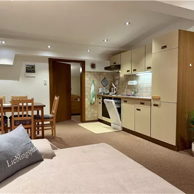 A cozy living room with a modern kitchen and a dining area. The space has a warm, inviting character.
