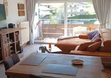 A bright living room with a cozy sofa and a dining table. Large windows offer a view of the surroundings and plenty of natural light.