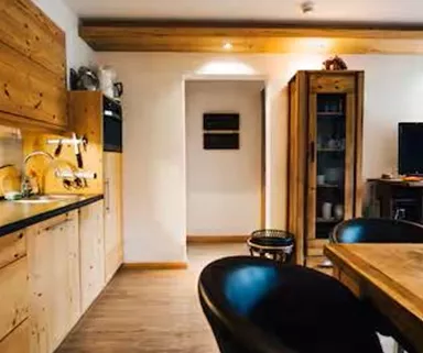 A modern kitchen with wooden furniture and a dining table. In the background, there is a television and there is an open space.