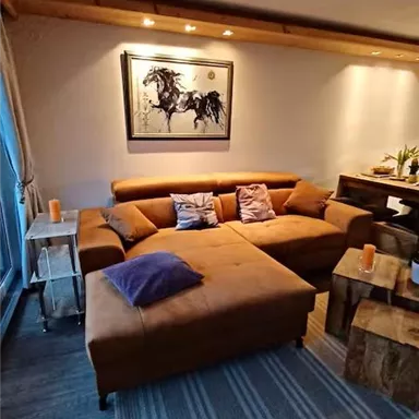 A cozy living room with a brown sofa and a piece of art on the wall. There are wooden details and candle-like decorations.
