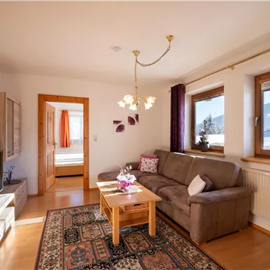 A cozy living room with a beige sofa, a wooden table, and an oriental carpet. Large windows offer a view of the mountains and flowing light.