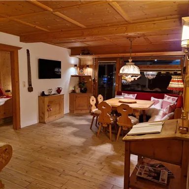 A cozy room with a wooden table and chairs. The walls are made of wood, and there is warm lighting.