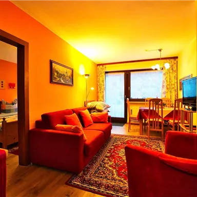 Eine gemütliche Wohnung mit roten Sofas und einem Essbereich. Die warmen Farben schaffen eine einladende Atmosphäre.
