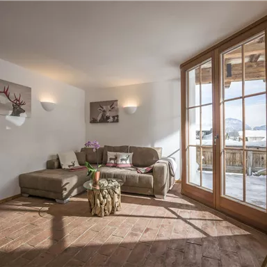 Ein gemütliches Wohnzimmer mit einem grauen Sofa und großen Fenstern, die auf einen Balkon führen. Der Raum verfügt über Holzfußboden und moderne Dekoration.