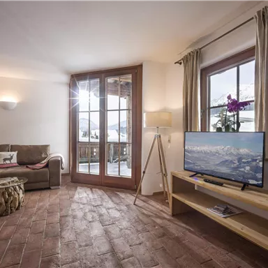 Ein einladendes Wohnzimmer mit einem großen Fenster, das viel Licht hereinscheinen lässt. Die Einrichtung besteht aus einer bequemen Couch, einem Fernseher und einem dekorativen Tisch.