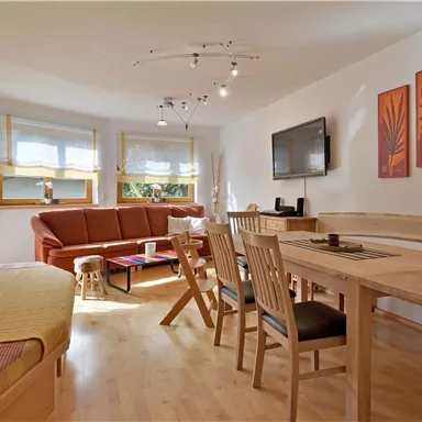 A bright and modern living kitchen with a cozy sofa and a dining area. Decorative pictures hang on the walls and there is a television.