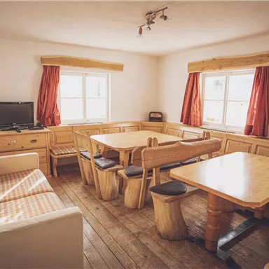 Ein gemütlicher Raum mit Holzmöbeln und großen Fenstern. Es gibt Sitzgelegenheiten und einen Fernseher.