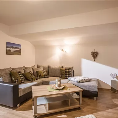 Ein gemütliches Wohnzimmer mit einer großen Couch und einem Holzkaffee-Tisch. Die Wände sind neutral gestaltet, und es gibt natürliche Lichtquellen.