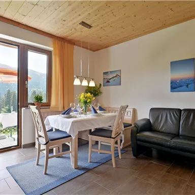 A cozy living space with a dining table and chairs. Large windows allow plenty of natural light in and offer a view of the surroundings.