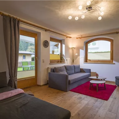 Ein modernes Wohnzimmer mit bequemen Sofas und einem kleinen Tisch. Große Fenster bieten viel Tageslicht und einen Blick auf die Umgebung.