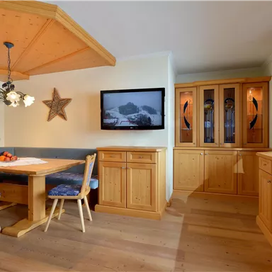 A cozy dining area with wooden furniture and a rounded ceiling. A television hangs on the wall, next to it is a showcase cabinet.