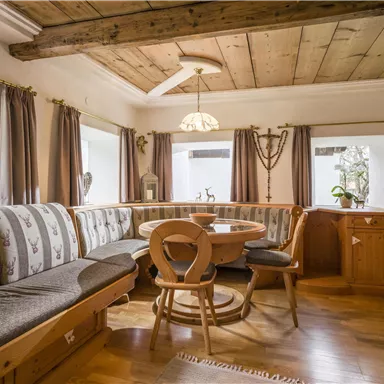 A cozy dining area with an L-shaped wooden bench and a round table. Large windows let in plenty of light and provide a view of the surroundings.