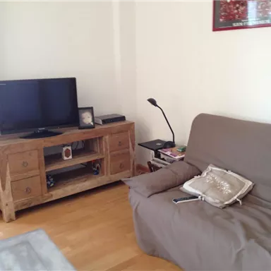 Ein gemütliches Wohnzimmer mit einem Sofa und einem Holzschrank. Ein Fernseher steht auf dem Schrank, und eine Lampe beleuchtet den Raum.