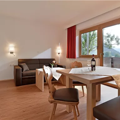 A bright apartment with modern furniture and a large window. The table is nicely set and a bottle of wine is ready.