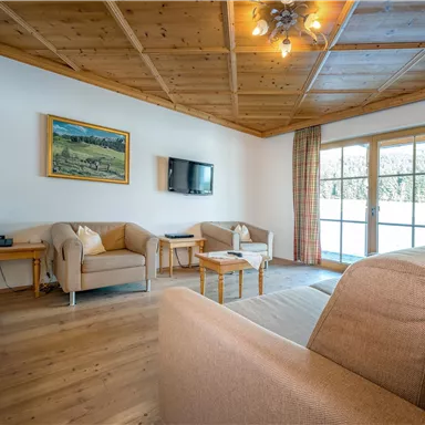A cozy living area with a bright sofa and comfortable armchairs. Large windows provide plenty of daylight and a view outside.