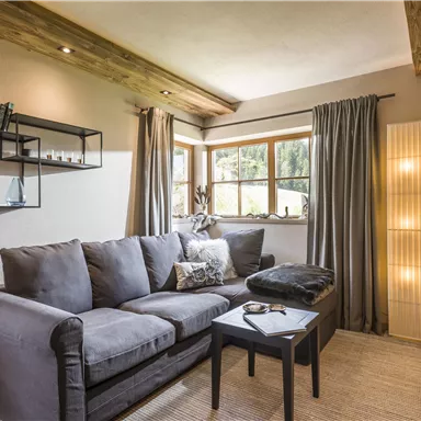 A cozy living room with a gray sofa and a small table. Large windows let in plenty of daylight, and modern decor gives the room style.