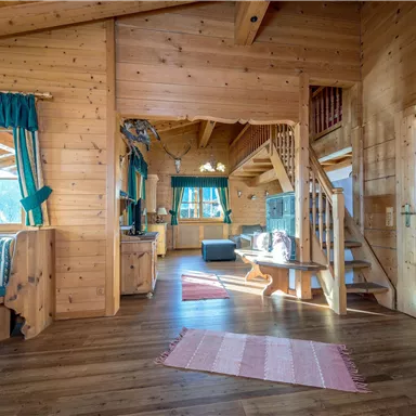 A cozy living space with wood paneling and bright light. The decor is rustic, featuring a staircase and large windows.