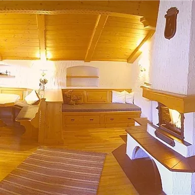 Ein gemütliches Wohnzimmer mit Holzvertäfelung und einem Kamin. Es gibt ein Essbereich und eine entspannte Sitzecke.