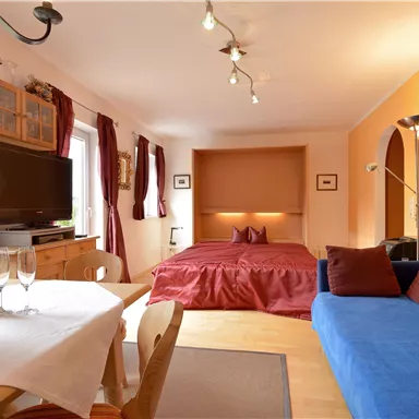Ein gemütliches Zimmer mit einem Doppelbett und einem blauen Sofa. Ein Tisch mit frischen Blumen und Getränken ergänzt die Ferienatmosphäre.