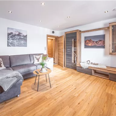A modern living room with a gray sofa, a small coffee table, and decorative elements. The floor is made of wood and there is a cozy atmosphere.