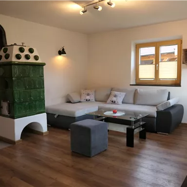 A cozy living space with a modern couch, a stylish table, and a traditional stove. The room has large windows that let in plenty of daylight.