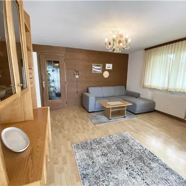 A bright living room with a gray sofa and a wooden table. Large windows ensure plenty of daylight and a cozy atmosphere.