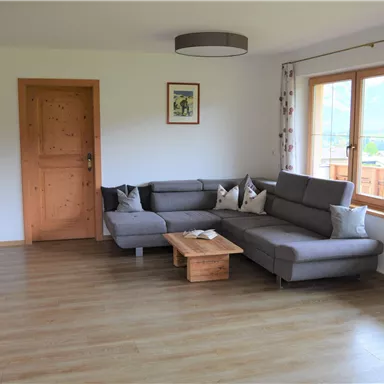 A bright living room with a gray sofa and a wooden coffee table. Large windows offer a view outside and let in plenty of light.