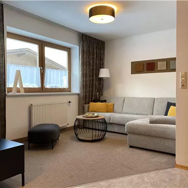A cozy living room with a gray sofa and a round coffee table. Large windows let in plenty of light and the decoration is modern and stylish.