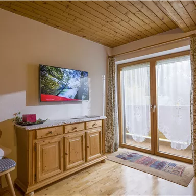 Ein gemütliches Zimmer mit einem Holzboden und vertäfelter Decke. Ein TV-Gerät und eine schöne Aussicht durch die Fenster sorgen für eine einladende Atmosphäre.