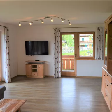 A modern living room with a television and large windows. The furniture is made of light wood and the atmosphere is bright and inviting.
