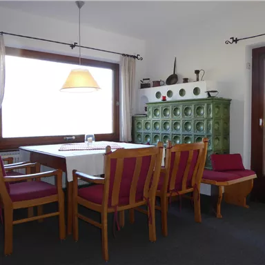 Ein gemütlicher Essbereich mit einem großen Tisch und sechs Stühlen. Eine grüne Kommode und ein Fenster lassen viel Licht herein.