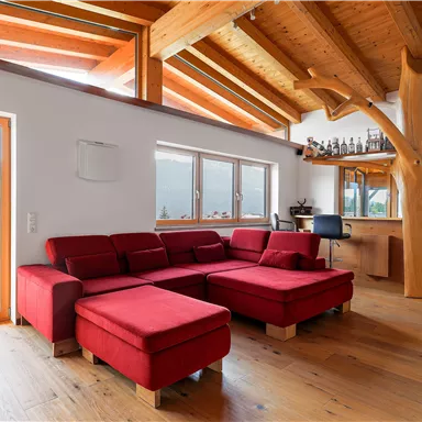 A modern living room with a red sofa and wooden beam ceiling. Large windows offer a view of the surrounding landscape.<br/>Featuring a cozy integrated bar.
