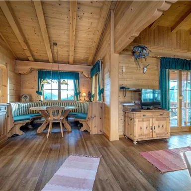 A cozy wooden apartment with an open living area. The furnishings are rustic and inviting, with a dining group and large windows.