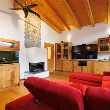 A modern living room with a red sofa and wooden walls. An aquarium, large TV, and a fireplace give the room a cozy atmosphere.
