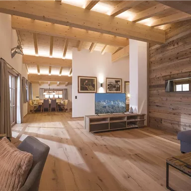 Ein modernes Wohnzimmer mit Holzdecke und einem großen Fernseher. Die Einrichtung ist gemütlich und einladend.