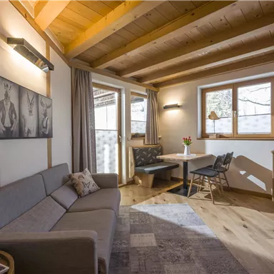 Ein gemütlicher Wohnraum mit Holzdecken und einem großen Fenster. Die Einrichtung umfasst ein Sofa, einen Esstisch und eine moderne Anrichte.