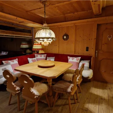 A cozy room with wooden paneling and a round table in the middle. Surrounding the table are chairs with fur covers and an inviting bench with cushions.