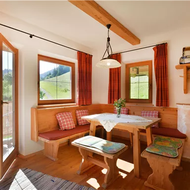An inviting living room with wood paneling and a cozy dining area. Large windows let in plenty of daylight and offer a view of the greenery.