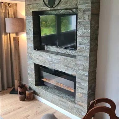 A modern living space with stone decor and a built-in television. At the lower level, there is a fireplace and a decorative wooden shelf.