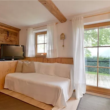 A cozy living space with a bright sofa and wooden walls. Large windows allow plenty of light and a view of the greenery.