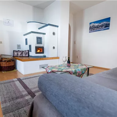 Ein gemütliches Wohnzimmer mit einem Holzofen und einer modernen Couch. An der Wand hängen Bilder, und der Raum ist gut beleuchtet.