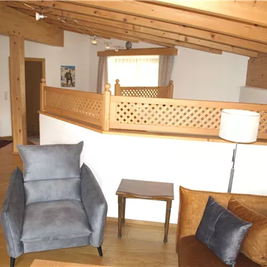 A cozy living room with wooden ceilings and modern furniture. There is a blue armchair and a brown couch in the room.