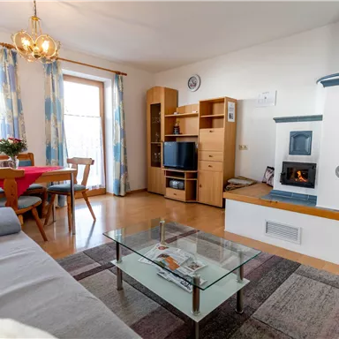 Ein gemütlicher Wohnraum mit einem Sofa, einem Glastisch und einem modernen Kamin. Der Raum ist hell und einladend, mit einem Essbereich und Fenstern, die viel Licht hereinlassen.