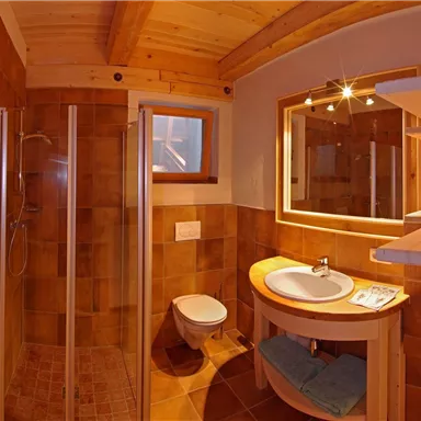 Ein modernes Badezimmer mit Holzverkleidung. Es enthält eine Dusche, ein Waschbecken und eine Toilette, alles in warmen Farben.