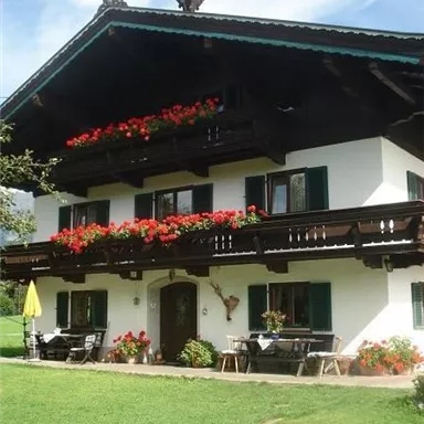 A traditional house with a balcony, adorned with red flowers. The garden is well-maintained and invites relaxation.