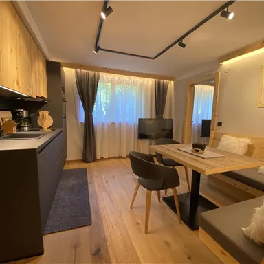 A modern kitchen with a dining area and cozy seating. The room is bright and welcoming, decorated in wood and gray tones.