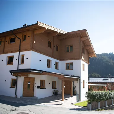 Ein modernes Gebäude im alpinen Stil mit Holzverkleidung. Die Umgebung ist von Bergen und klarer Bläue umgeben.